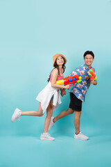 Side view of full length portrait of Young Asian couple walking and holding water gun isolated on...