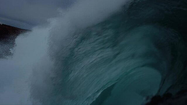 Lip of wave comes crashing down on ocean water, view down barrel tube
