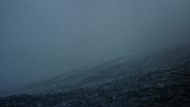 Ocean water spray and mist blows over top of wave on stormy day, slow motion in water