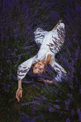 On a lavender field, a young woman lying in a white dress lies on the ground in the middle of it