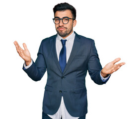 Hispanic man with beard wearing business suit and tie clueless and confused expression with arms...