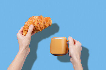 Women's hands hold fresh croissant and cup of coffee  on a blue background. Design concept for breakfast pastry mockup or banner.