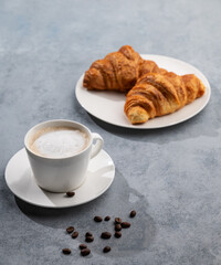 A cup of aromatic cappuccino coffee and fresh croissants on a blue background with coffee beans.
