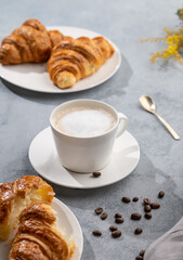 A cup of aromatic cappuccino coffee and fresh croissants on a blue background with coffee beans and flowers.