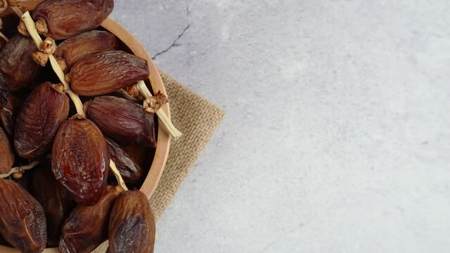overhead midsection shot of a wooden bowl of date palm fruits rotate on stone table