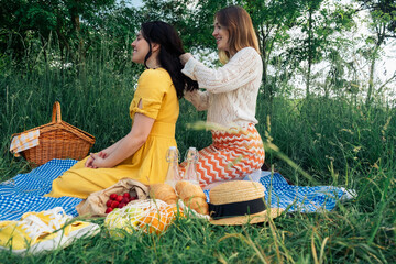 Braiding friendship: young woman styles friend's hair at picnic.