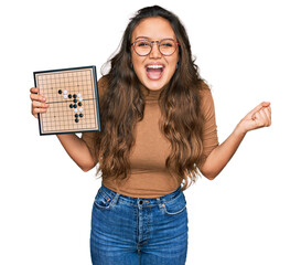 Young hispanic girl holding drauhgts screaming proud, celebrating victory and success very excited...