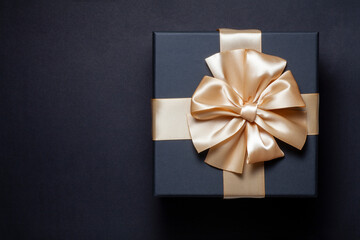 Black gift box with champagne gold ribbon bow on a black background. top view