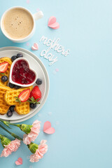 Mother's Day brunch layout: overhead vertical shot of a table with heart waffles, berries, syrup, coffee, carnations, 
