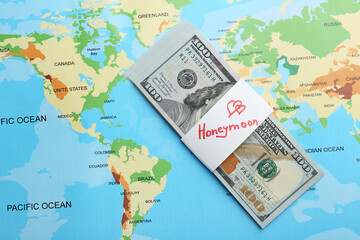 Stack of money with word Honeymoon on world map, top view