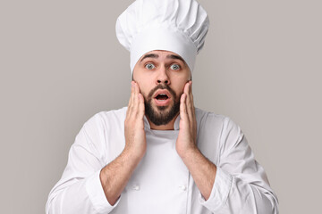 Surprised young chef in uniform on grey background