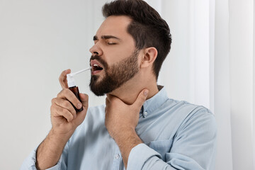 Young man using throat spray at home