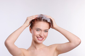 Naklejka premium Happy young woman washing her hair with shampoo on light grey background