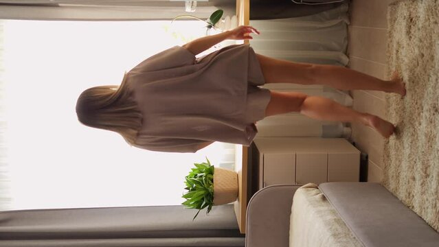 A woman dances to the music by the window, swaying to the rhythm and letting the music guide her movements. The music sets the mood, creating an atmosphere of freedom and expression.