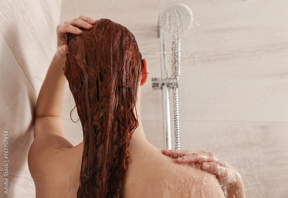 Sticker Young woman washing her hair with shampoo in shower, back view