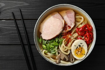 Delicious ramen in bowl and chopsticks on black wooden table, flat lay. Noodle soup