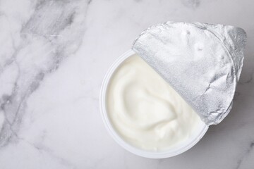 Delicious natural yogurt in plastic cup on white marble table, top view. Space for text