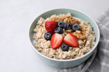 Tasty oatmeal with strawberries, blueberries and walnuts in bowl on grey table