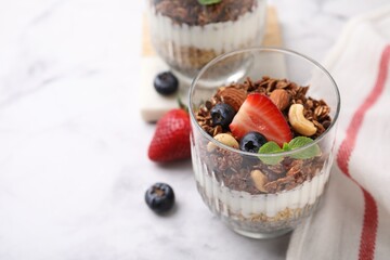 Tasty granola with berries, nuts and yogurt in glass on white marble table, closeup. Space for text