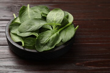 Fresh spinach leaves in bowl on wooden table, closeup