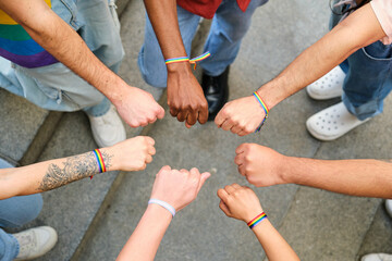 A group of multiracial people with rainbow LGBTQ bracelets standing in a circle. Scene is one of unity and solidarity.
