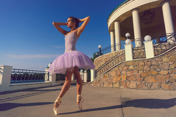 young ballerina in a tutu and pointe shoes with beautiful feet dances on a summer day in a pavilion on the terrace