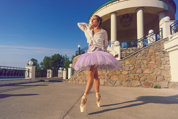 young ballerina in a tutu and pointe shoes with beautiful feet dances on a summer day in a pavilion...