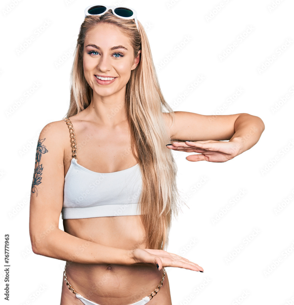 Wall mural Beautiful young blonde woman wearing bikini gesturing with hands showing big and large size sign, measure symbol. smiling looking at the camera. measuring concept.