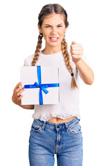 Beautiful caucasian woman with blonde hair holding gift annoyed and frustrated shouting with anger, yelling crazy with anger and hand raised