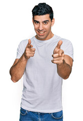 Handsome hispanic man wearing casual white t shirt pointing fingers to camera with happy and funny face. good energy and vibes.