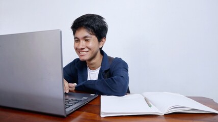 Fototapeta na wymiar Young handsome Asian male student is happy studying at a table using a book and laptop
