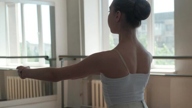 A ballerina in a white tutu trains and dances beautifully.