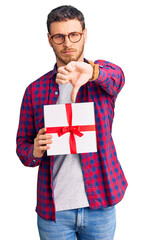 Handsome young man with bear holding gift with angry face, negative sign showing dislike with thumbs down, rejection concept