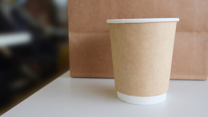 Brown paper cup placed on table, with a takeaway paper bag in the background.