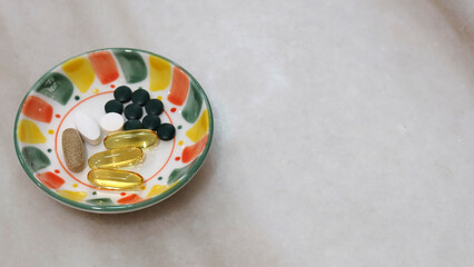 A small plate with various health supplement pills and capsules. On a marble surface, with copy space on the right.