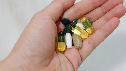 Closeup of hand holding assorted supplement pills and capsules. 