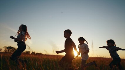 Children running in park at sunset. happy family kindergarten kids dream concept. Kids running in grass silhouette. Children lifestyle playing outdoors silhouette. Kids playing in the park at sunrise - 767789990