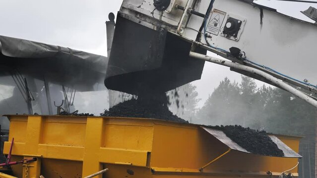 Loading hot asphalt into paver, pouring hot asphalt crumbs in asphalt spreader
