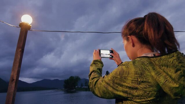Woman taking picture with smartphone. Evening shot against the backdrop of an evening mountain lake.