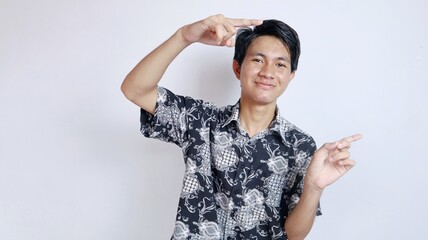 young handsome Asian student male happy wearing batik pointing to the side