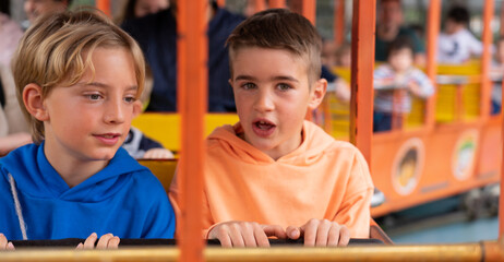 Two Caucasian children riding a train ride at an amusement park