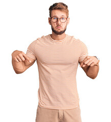 Young caucasian man wearing casual clothes and glasses pointing down looking sad and upset,...
