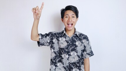 Excited handsome young Asian man wearing batik cloth gesturing upwards