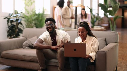 Creative Team Engaged in a Lively Discussion Over Laptop - Colleagues laugh and discuss a project, gathered around a laptop in a light-filled workspace.