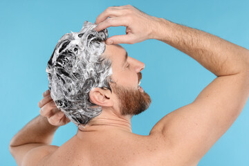 Man washing his hair with shampoo on light blue background, back view