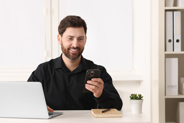 Smiling man using smartphone at table in office