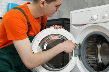 Young plumber repairing washing machine in bathroom