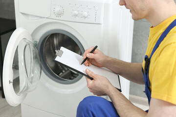 Plumber writing results of examining washing machine in bathroom, closeup - obrazy, fototapety, plakaty