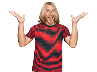 Caucasian man with blond long hair wearing casual striped t shirt celebrating crazy and amazed for success with arms raised and open eyes screaming excited. winner concept