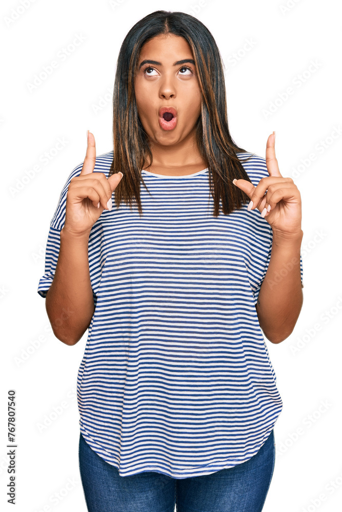 Sticker young latin girl wearing casual clothes amazed and surprised looking up and pointing with fingers an